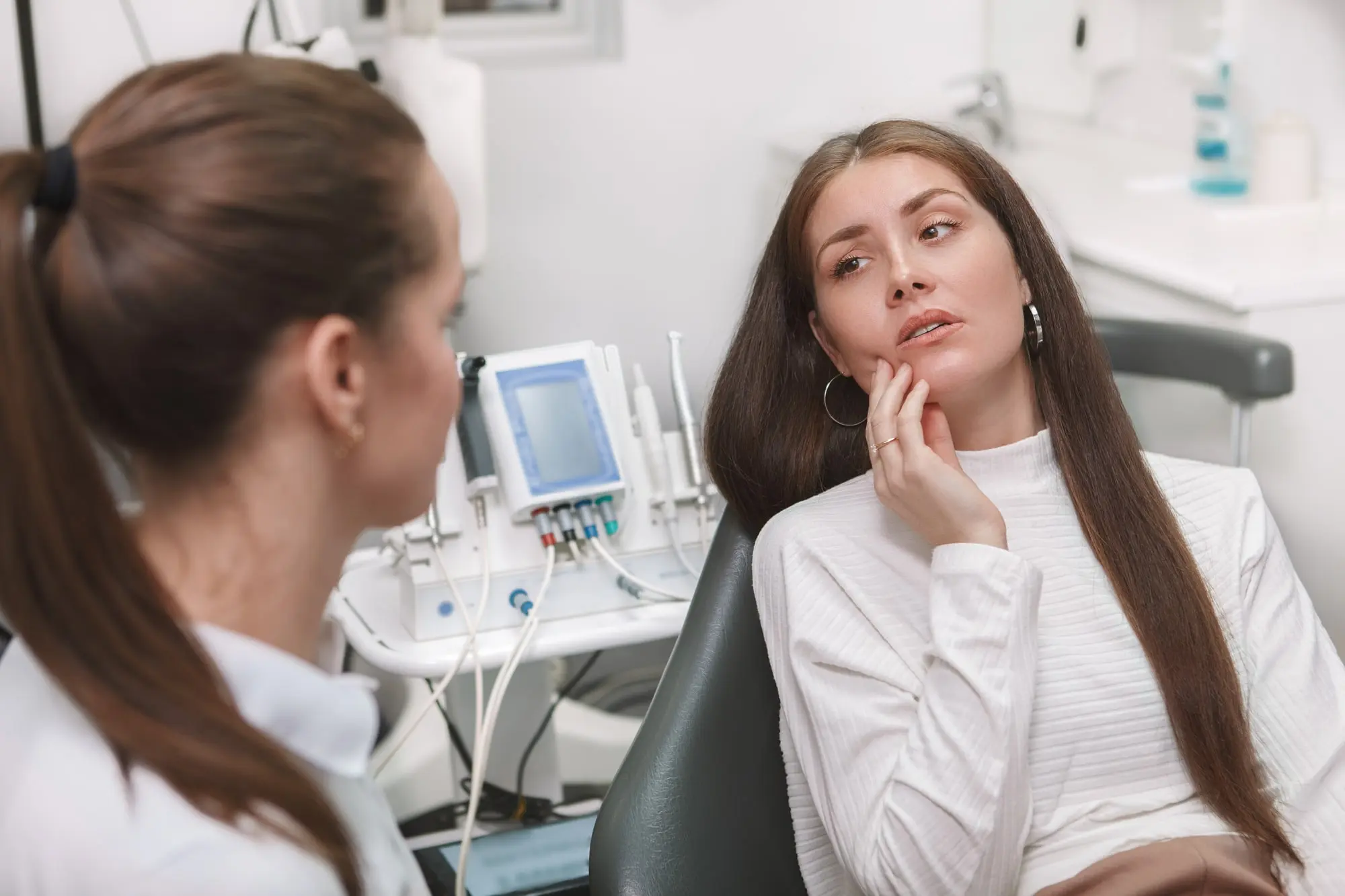 A young woman at the dentist holding her cheek while a dentist listens to her