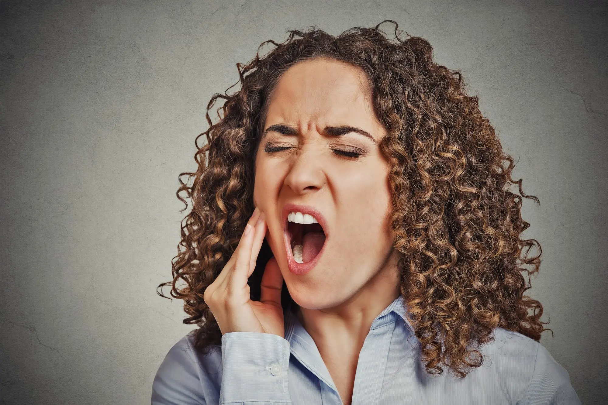 A woman holding her hand to her cheek wincing in pain