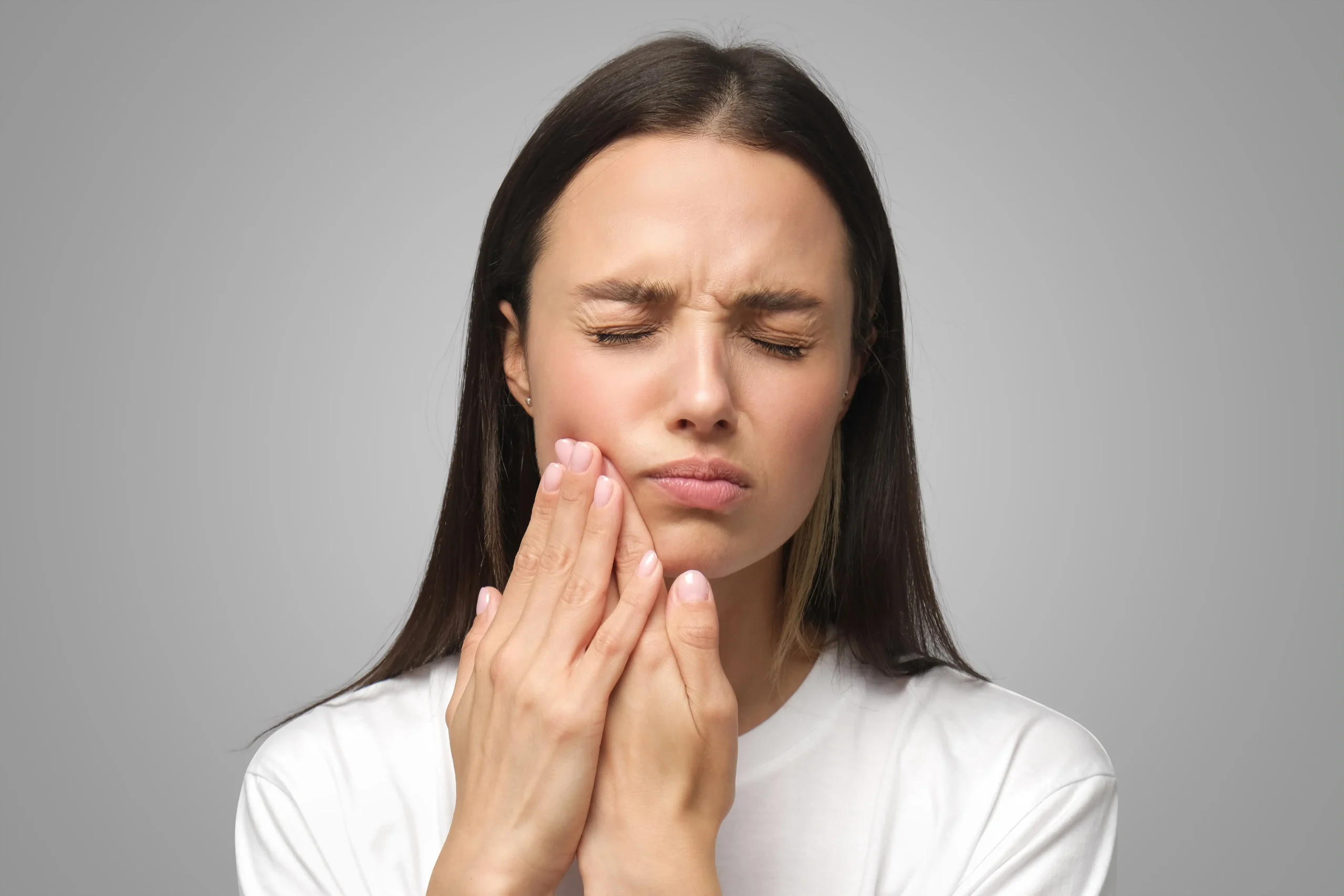 A young woman with her eyes closed holding her hand to her cheek in pain.