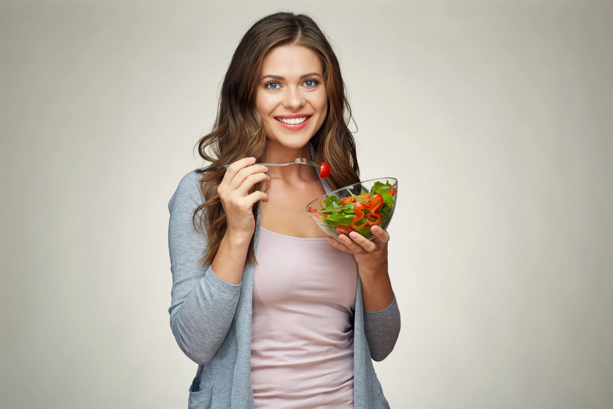 A woman holding a fork and a bowl of salad while smiling