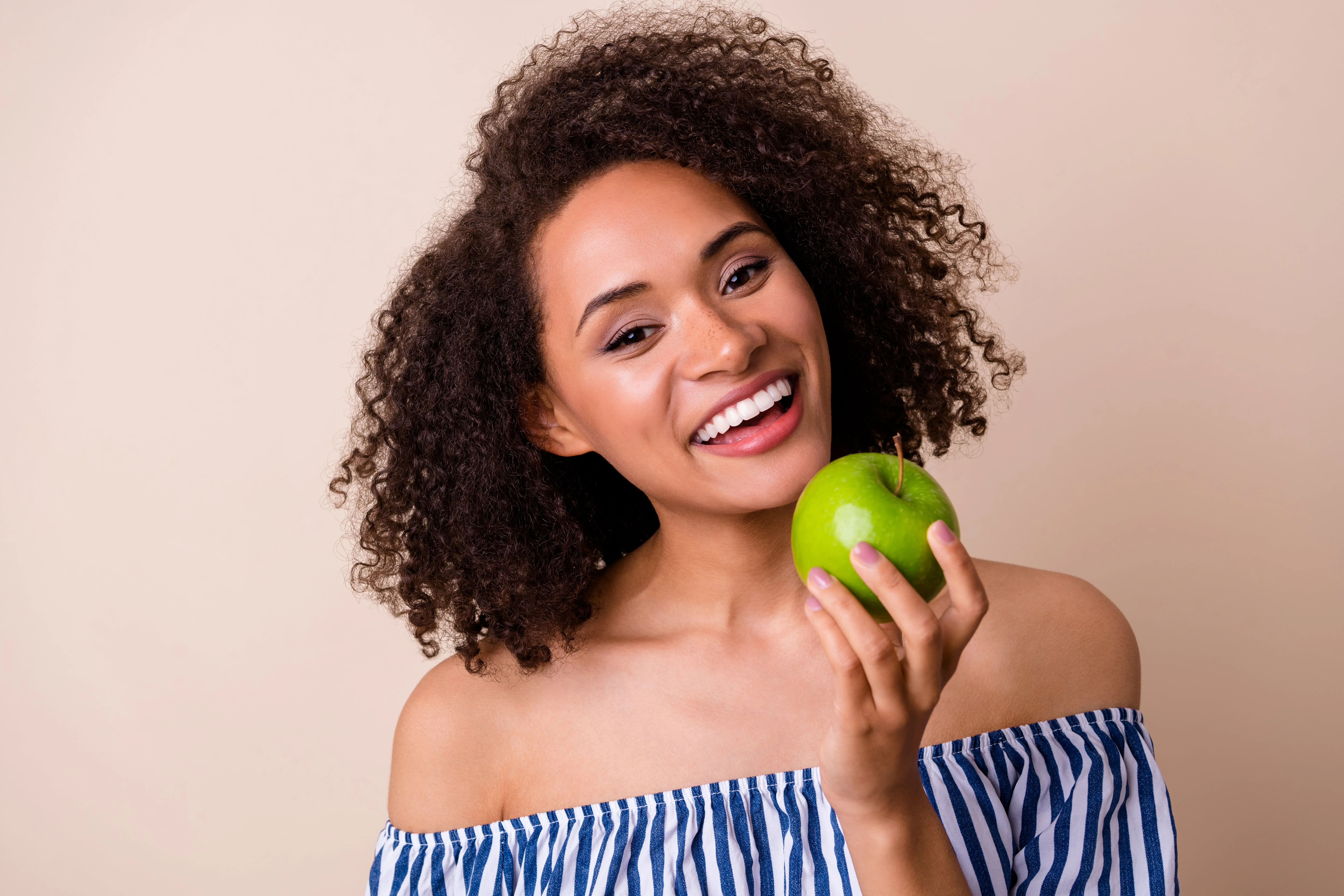A brown skinned girl smiling and holding an apple.
